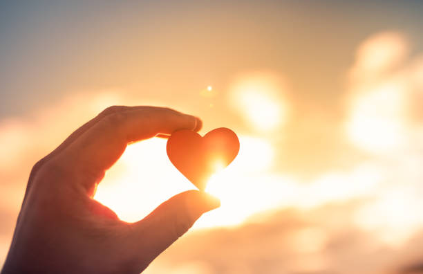 Hand Holding Red Heart Against A Beautiful Sunset.